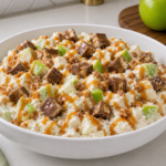 Apple Snickers Salad in a white bowl with green apples, chopped candy, toffee bits, and caramel drizzle.