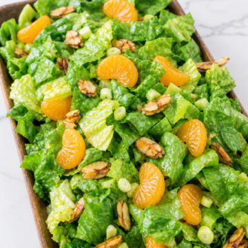 Mandarin orange salad with romaine, candied almonds, celery, green onions, and vinaigrette in a wooden bowl