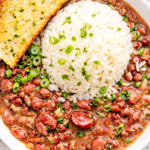 Cajun red beans and rice served in a white bowl with fluffy white rice, sliced green onions, and garlic bread on the side
