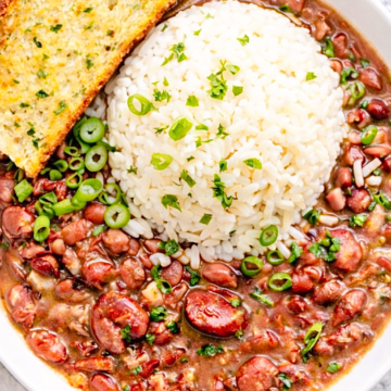 Cajun red beans and rice served in a white bowl with fluffy white rice, sliced green onions, and garlic bread on the side