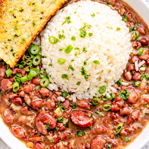 Cajun red beans and rice served in a white bowl with fluffy white rice, sliced green onions, and garlic bread on the side