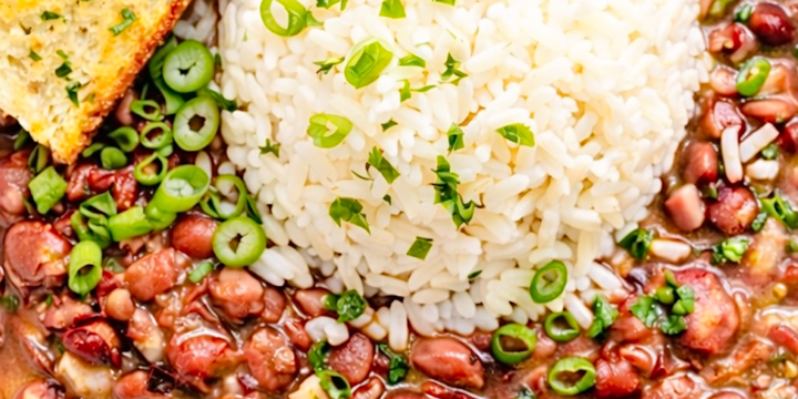 Cajun red beans and rice served in a white bowl with fluffy white rice, sliced green onions, and garlic bread on the side