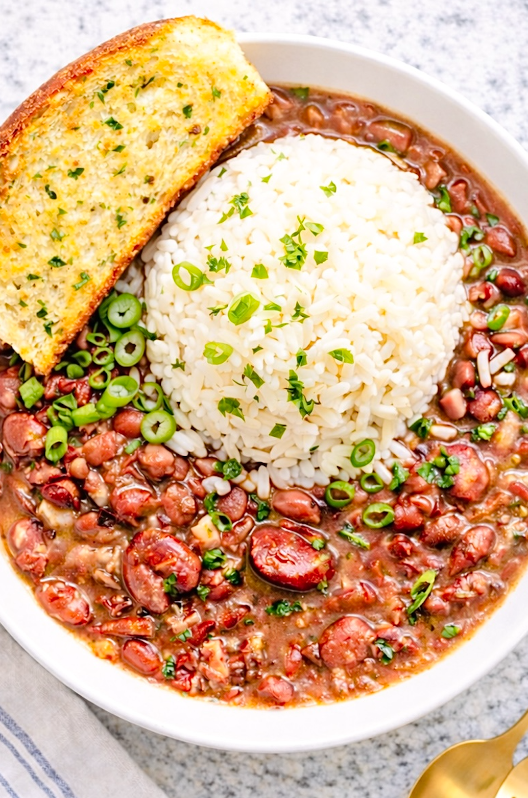 Cajun red beans and rice served in a white bowl with fluffy white rice, sliced green onions, and garlic bread on the side