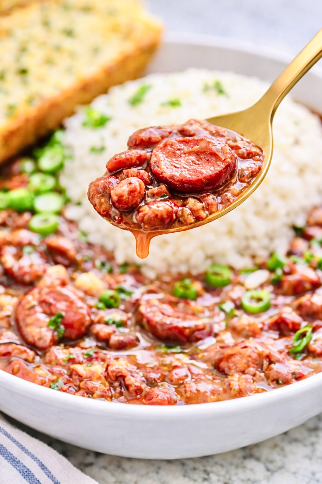 Spoonful of creamy Cajun red beans and Andouille sausage dripping over a bowl of red beans and rice