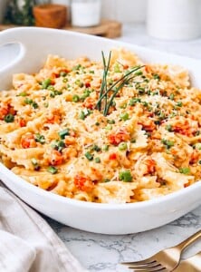 Creamy crawfish pasta with bow tie noodles in a white baking dish, topped with chopped green onions and grated Parmesan cheese.