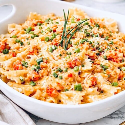 Creamy crawfish pasta with bow tie noodles in a white baking dish, topped with chopped green onions and grated Parmesan cheese.