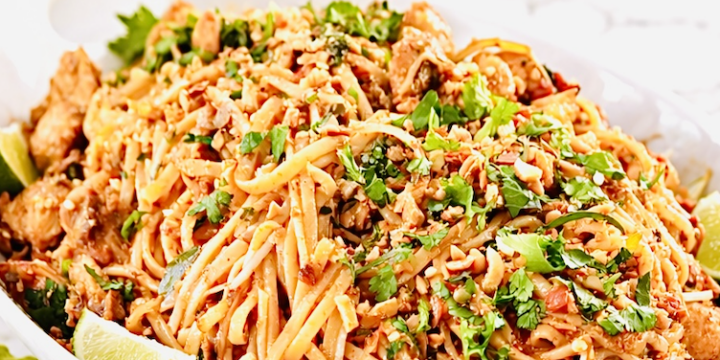 chicken pad thai noodles with lime wedges, crushed peanuts, cilantro, and golden fork on white serving platter
