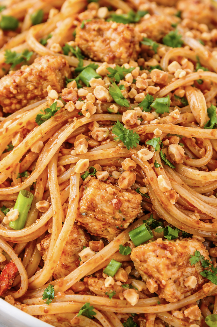 close up of chicken pad thai noodles coated in sauce with chopped peanuts, scallions, cilantro, and chicken pieces