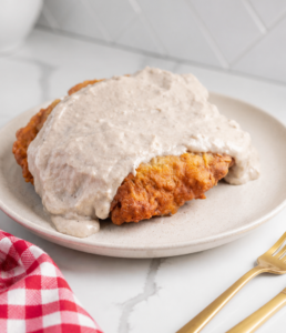 Crispy chicken fried steak covered with peppered cream gravy on a white ceramic plate.