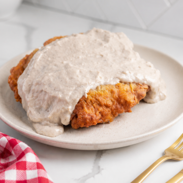 Crispy chicken fried steak covered with peppered cream gravy on a white ceramic plate.