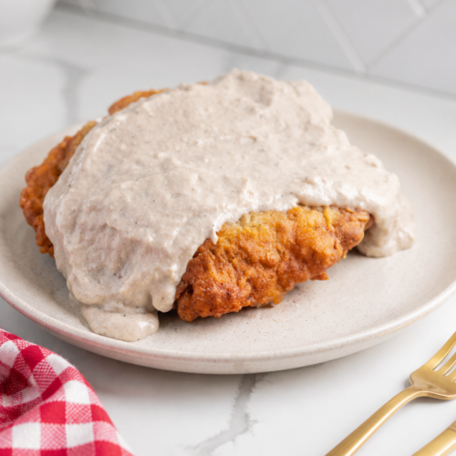 Crispy chicken fried steak covered with peppered cream gravy on a white ceramic plate.