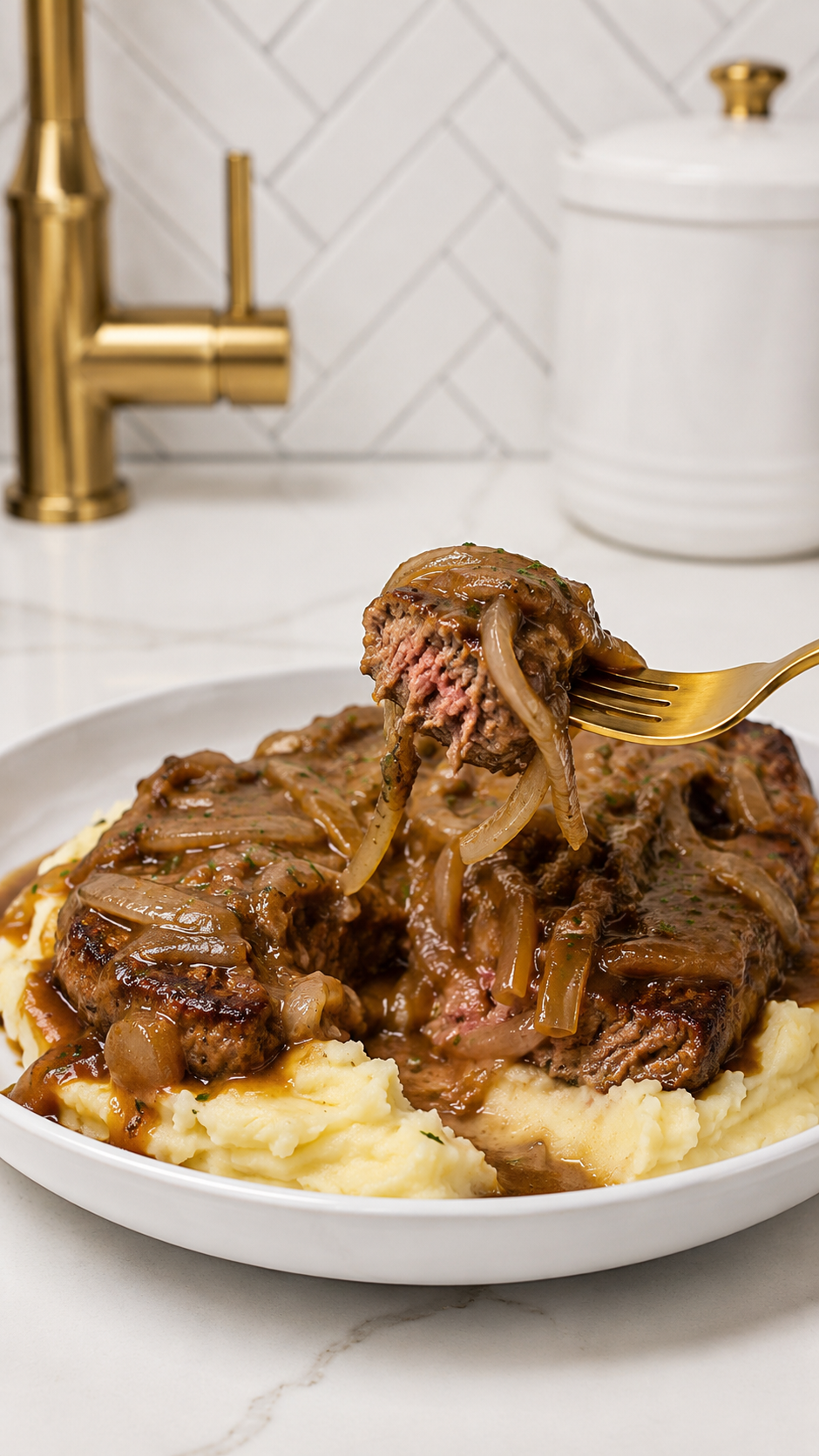 Gold fork lifting a bite of smothered steak with onion gravy from a plate of creamy mashed potatoes.