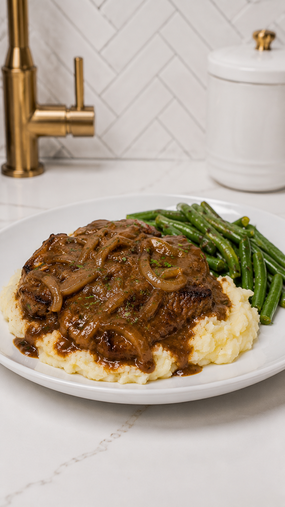 Smothered steak with rich onion gravy served over mashed potatoes with seasoned green beans on a white dinner plate.