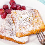 easy french toast dusted with powdered sugar on a plate with a side of grapes