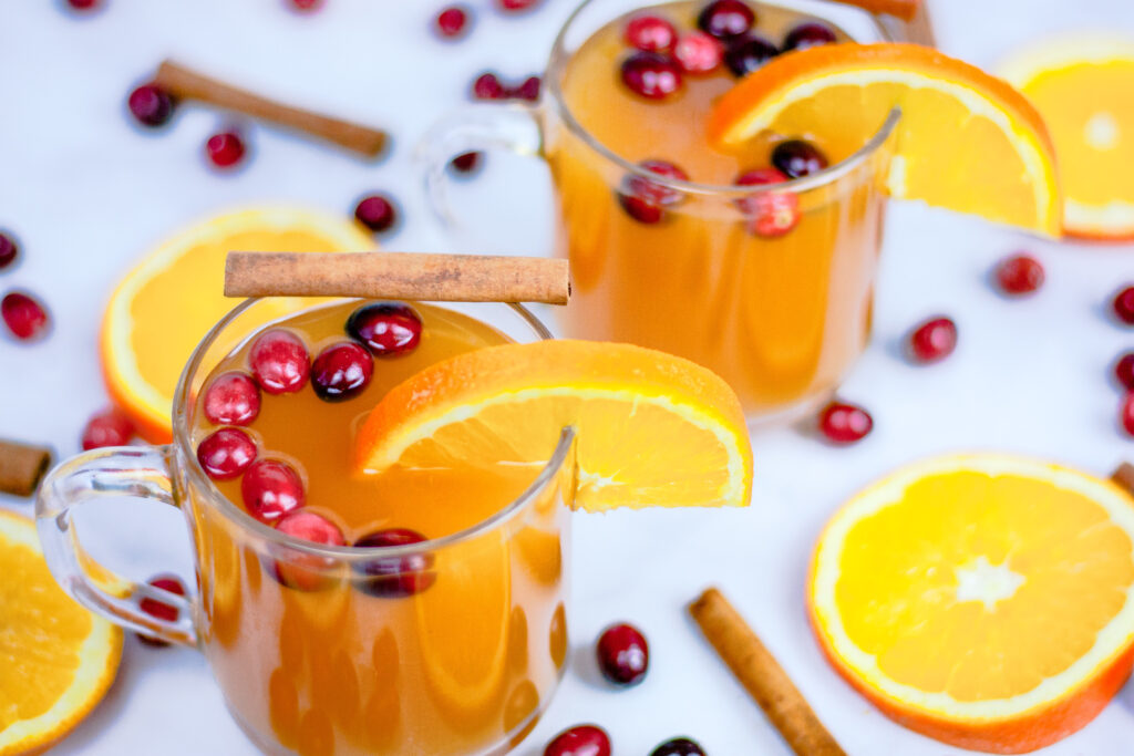 Cups of steaming spiced tea with oranges and cranberries garnishing the top