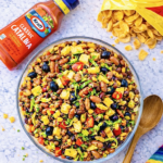 Overhead view of Catalina taco salad with ground beef, Fritos, kidney beans, black olives, corn, tomatoes, and shredded lettuce in a large glass serving bowl
