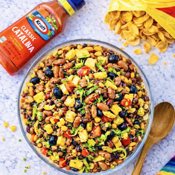 Overhead view of Catalina taco salad with ground beef, Fritos, kidney beans, black olives, corn, tomatoes, and shredded lettuce in a large glass serving bowl