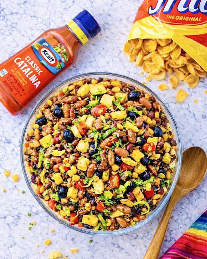 Overhead view of Catalina taco salad with ground beef, Fritos, kidney beans, black olives, corn, tomatoes, and shredded lettuce in a large glass serving bowl