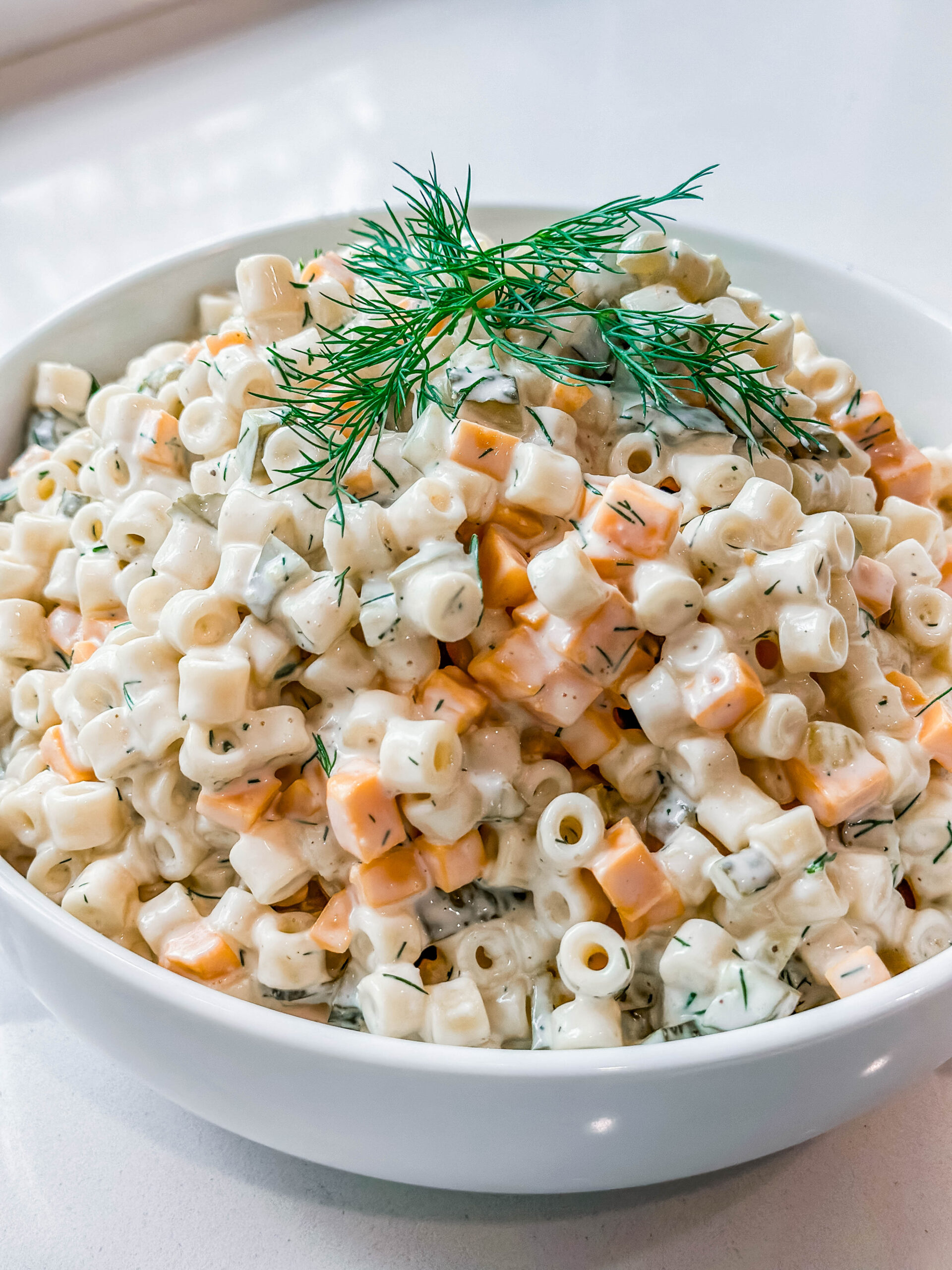 Creamy Dill Pickle Pasta Salad In a white serving bowl, garnished with fresh sprigs of dill. 