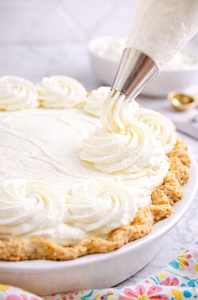 Piping stabilized whipped cream rosettes onto a cream pie using a metal pastry tip, demonstrating bakery-style whipped cream that holds its shape.