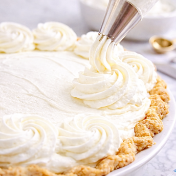 Piping stabilized whipped cream rosettes onto a cream pie using a metal pastry tip, demonstrating bakery-style whipped cream that holds its shape.
