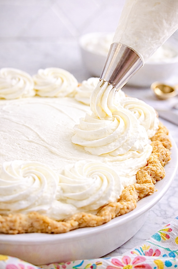 Piping stabilized whipped cream rosettes onto a cream pie using a metal pastry tip, demonstrating bakery-style whipped cream that holds its shape.