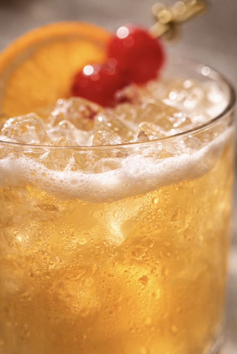Extreme close-up of whiskey sour showing frothy top, fresh ice, and citrus garnish detail