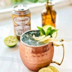 An icy mug of Moscow Mule garnished with a sprig of fresh mint, fresh lime wheel, and candied ginger.
