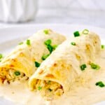 Close-up of creamy white chicken enchiladas with salsa verde sauce and green onions on a white plate