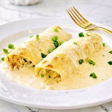 Creamy white chicken enchiladas topped with salsa verde sauce on a white plate with gold fork and bright kitchen background