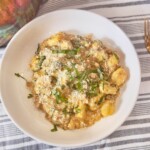 Bowl of savory pumpkin sausage gnocchi with caramelized mushrooms, garnished with fresh basil and Parmesan cheese.
