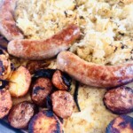 A full sheet pan dinner with bratwurst, sauerkraut, sliced onions, and crispy roasted potatoes, ready to serve