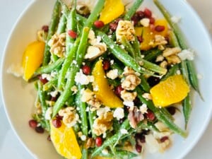 Cold Green Bean Salad with Citrus Vinagrette and garnished with orange supremes, blue cheese, toasted walnuts, and pomegranate arils.