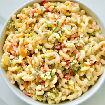 Bowl of creamy macaroni salad with elbow pasta, red peppers, celery, and chopped eggs, garnished with green onions and served on a rustic picnic table—perfect for summer potlucks and backyard BBQs.