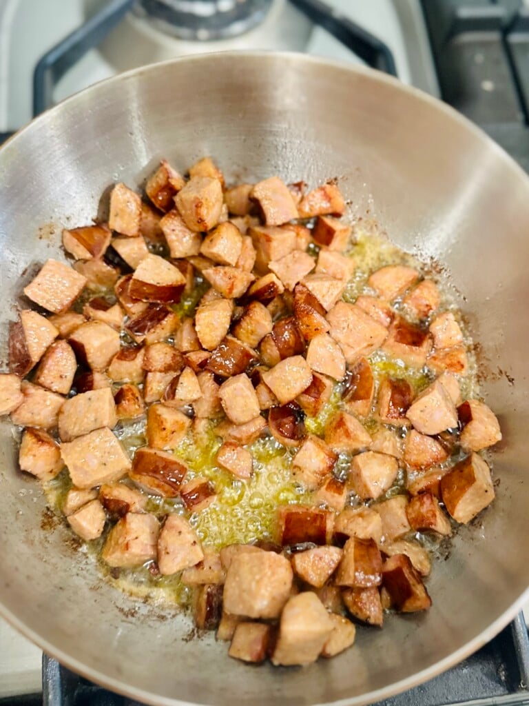 Adding Andouille sausage to the bacon in a skillet for shrimp and sausage jambalaya