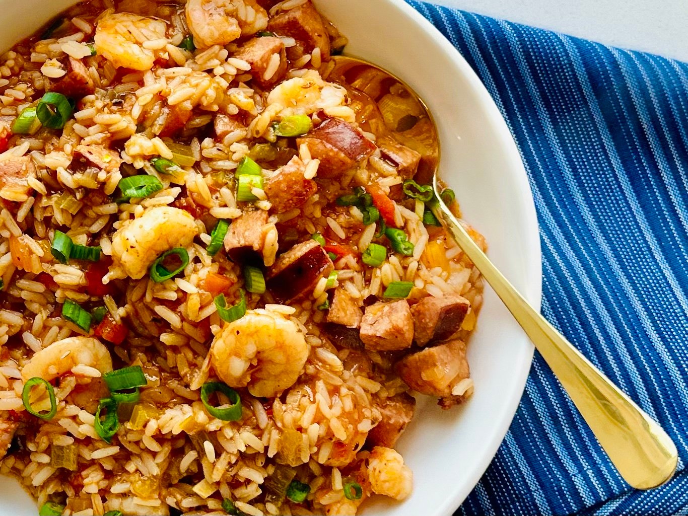Sausage and shrimp jambalaya served in a white bowl with green onions