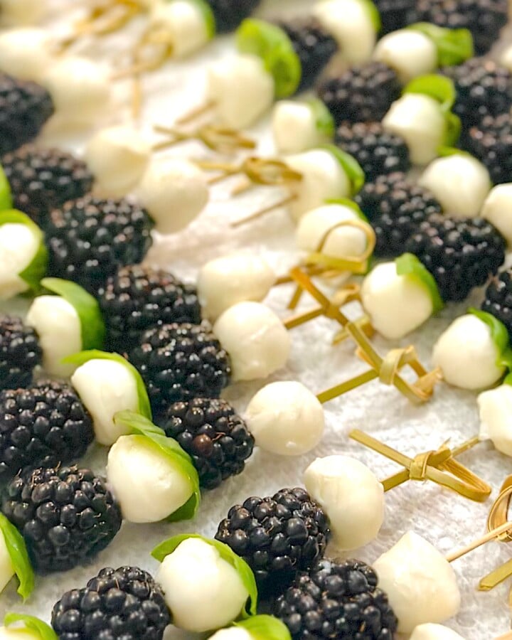 Close-up of blackberry caprese skewers with fresh basil, mozzarella balls, and juicy blackberries drizzled with balsamic glaze.