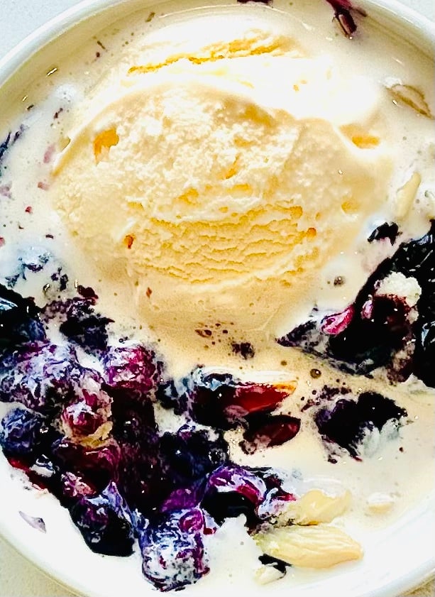 Slice of blueberry cobbler dump cake on a plate with melting ice cream