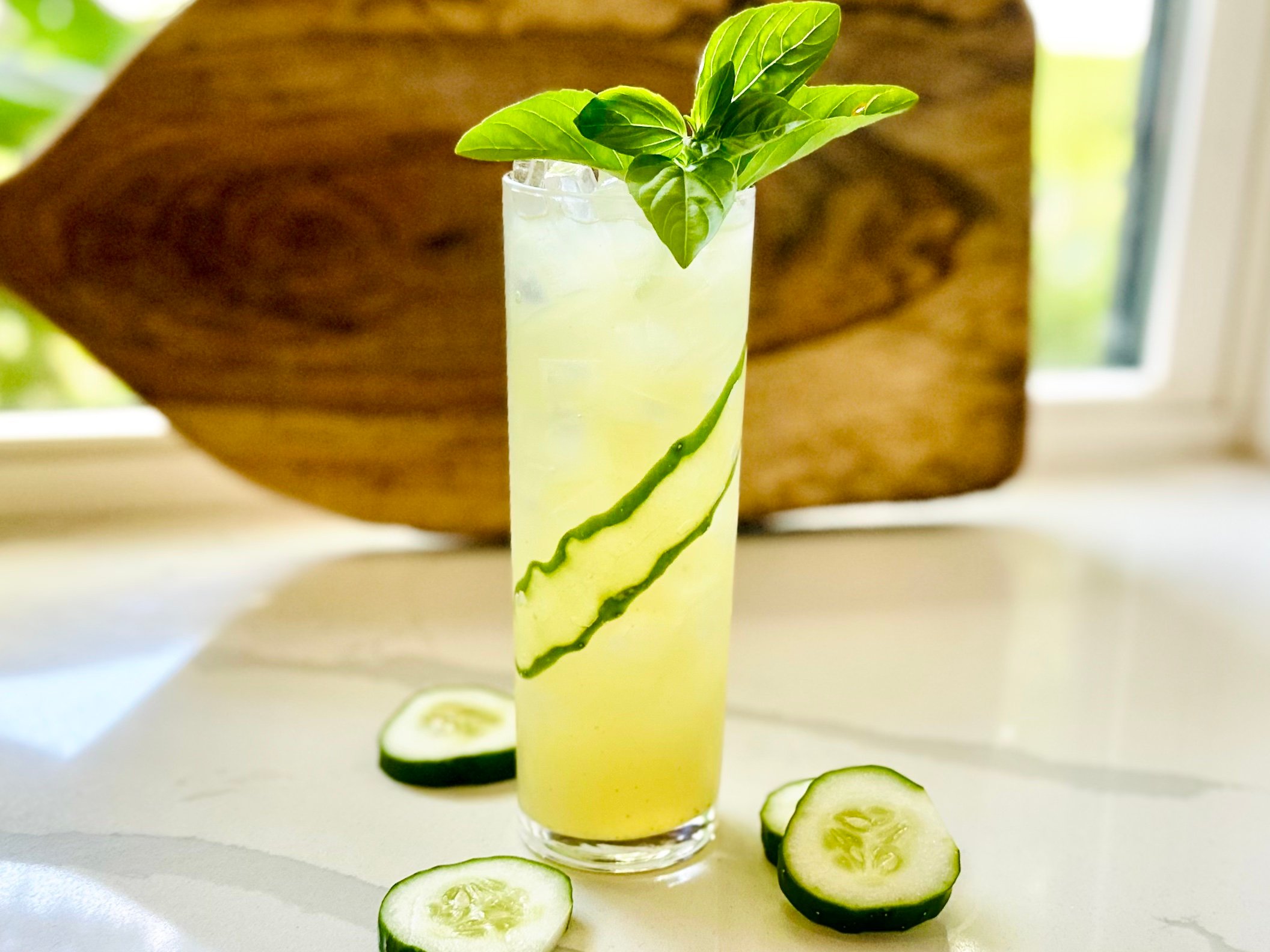 Garden Gimlet cocktail in a highball glass with fresh basil and cucumber ribbon garnish, served over ice.