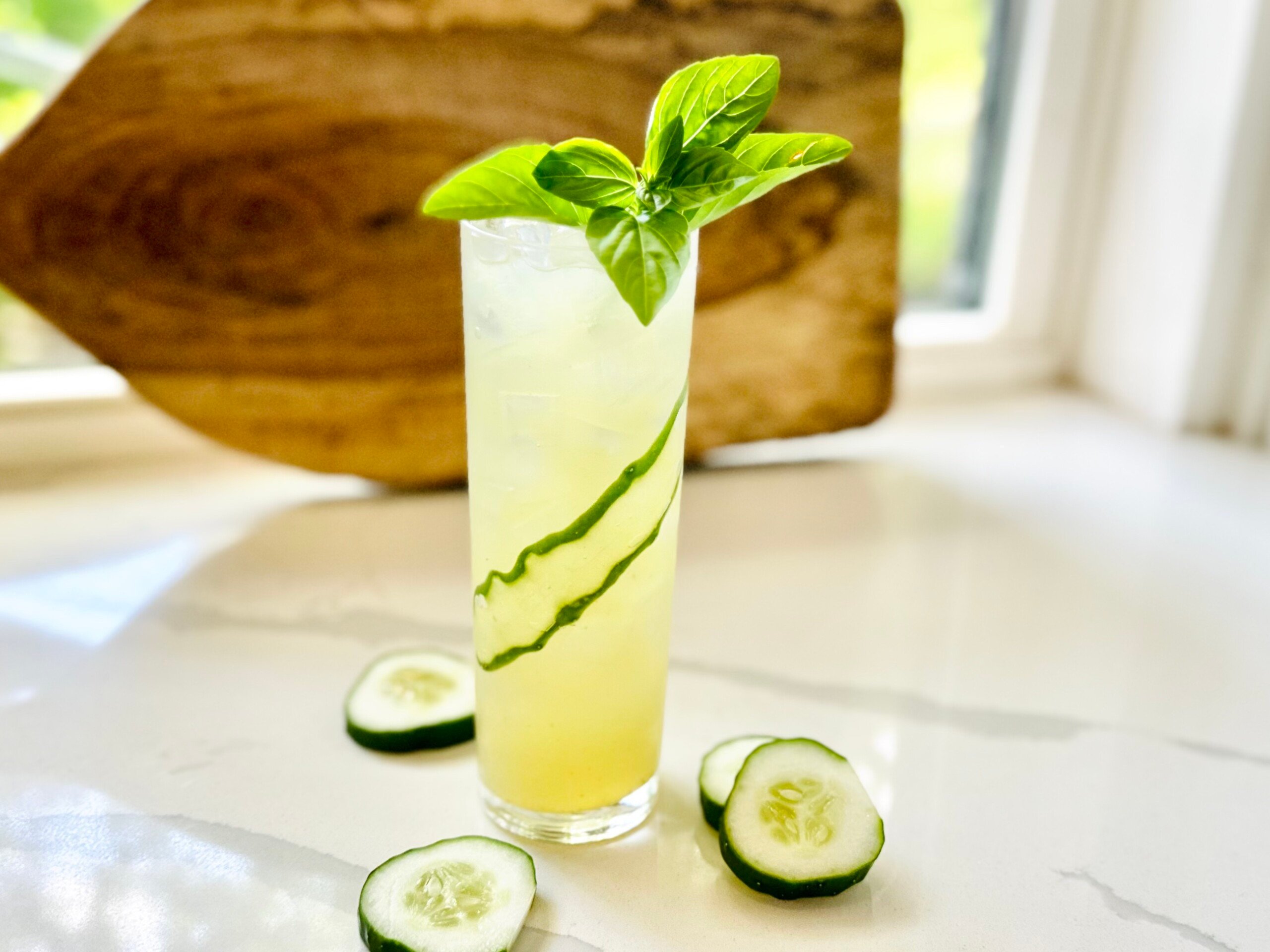 Refreshing herb-infused gimlet in a tall highball glass, topped with basil leaves and cucumber ribbon.