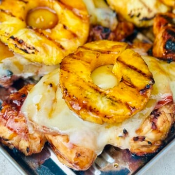 Close-up of grilled chicken layered with prosciutto, Gruyère cheese, and pineapple ring