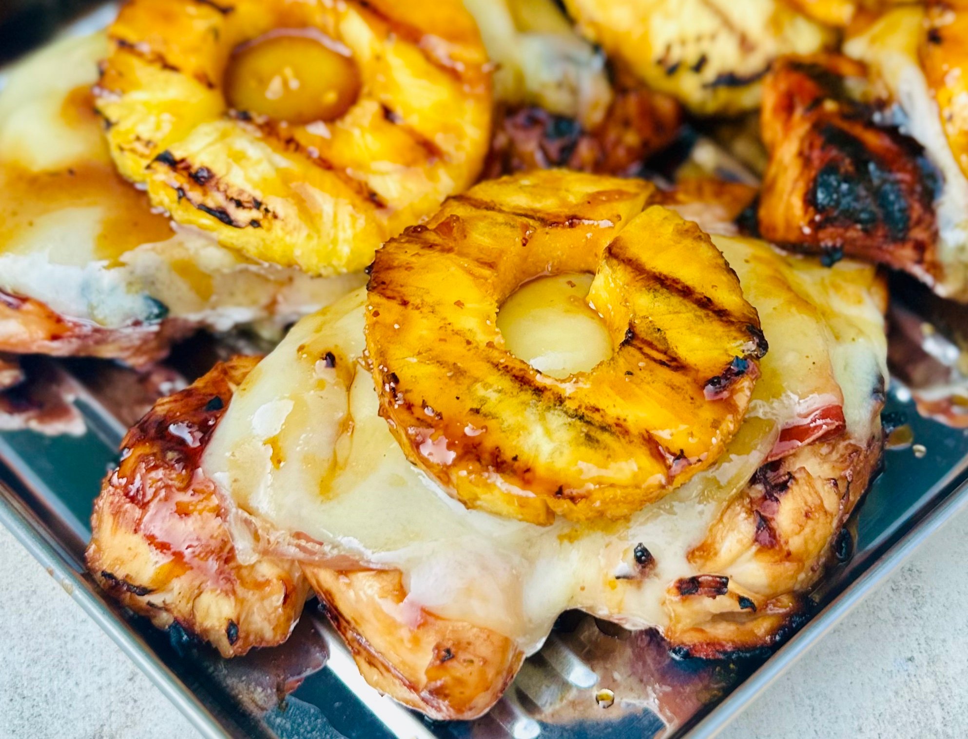 Close-up of grilled chicken layered with prosciutto, Gruyère cheese, and pineapple ring