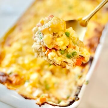 Serving spoon lifting hearty chicken cobbler with vegetables and biscuits