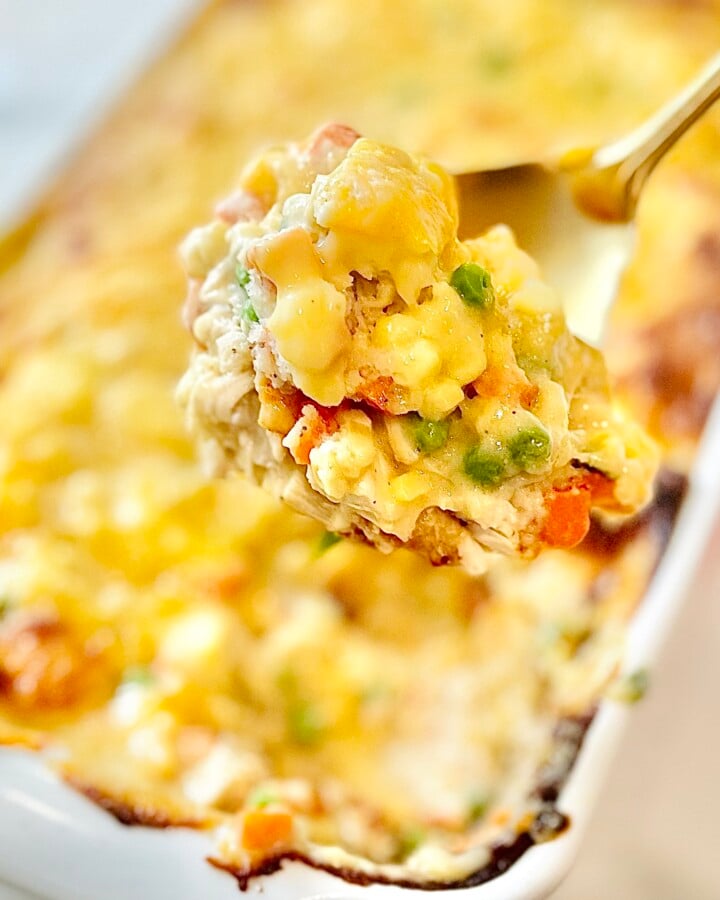 Serving spoon lifting hearty chicken cobbler with vegetables and biscuits