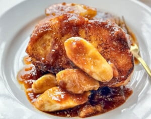 Thick slices of French toast topped with caramelized bananas and rich rum sauce on a white plate