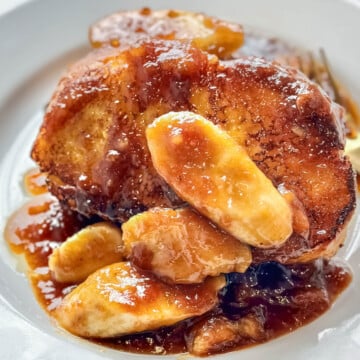 Thick slices of French toast topped with caramelized bananas and rich rum sauce on a white plate