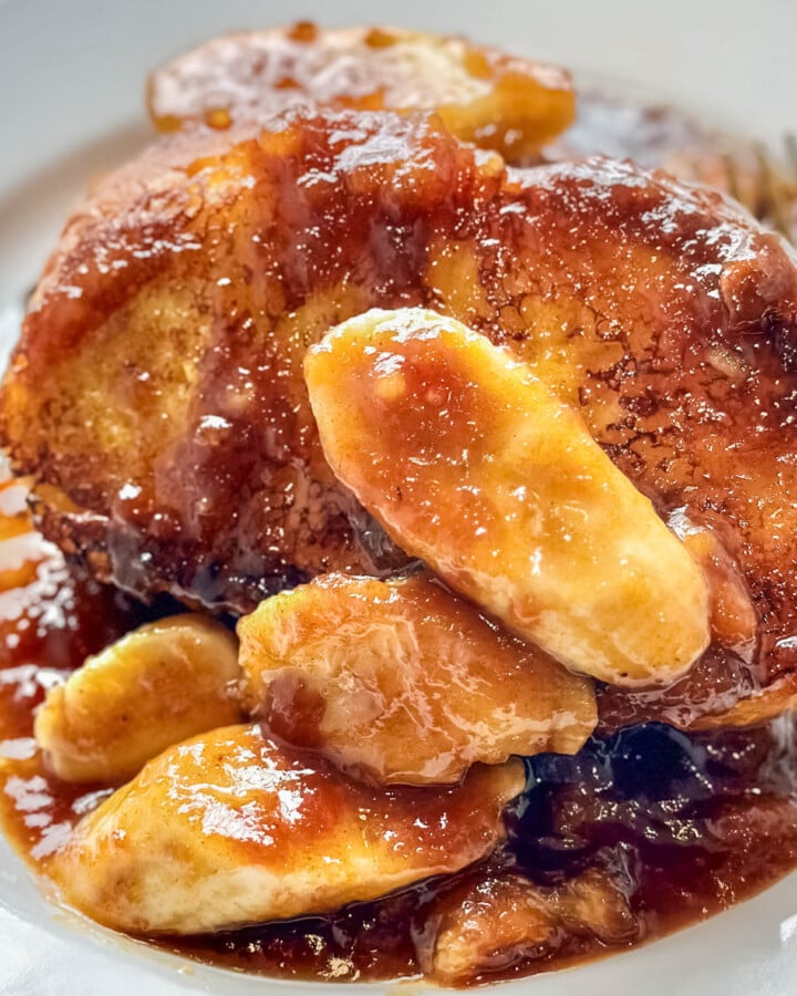 Thick slices of French toast topped with caramelized bananas and rich rum sauce on a white plate
