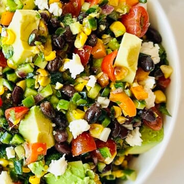 Fresh avocado, corn, black beans, and tomatoes mixed into a Mexican chopped salad in a white serving bowl