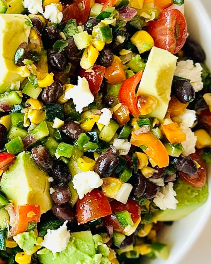 Fresh avocado, corn, black beans, and tomatoes mixed into a Mexican chopped salad in a white serving bowl