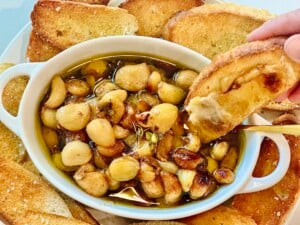 Rustic appetizer of garlic confit in baking dish with toasted baguette